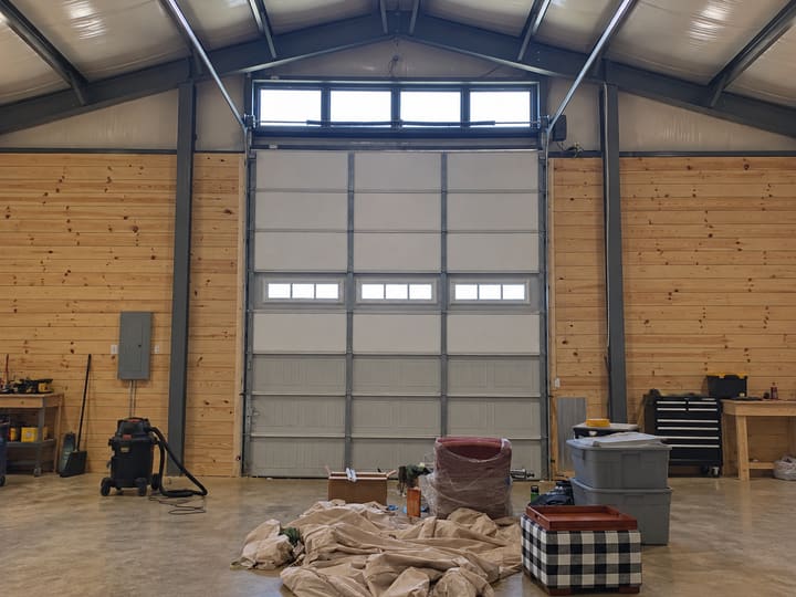 Garage door partway through insulation: the upper sections have white vinyl-backed panels while the bottom three sections still show the bare steel